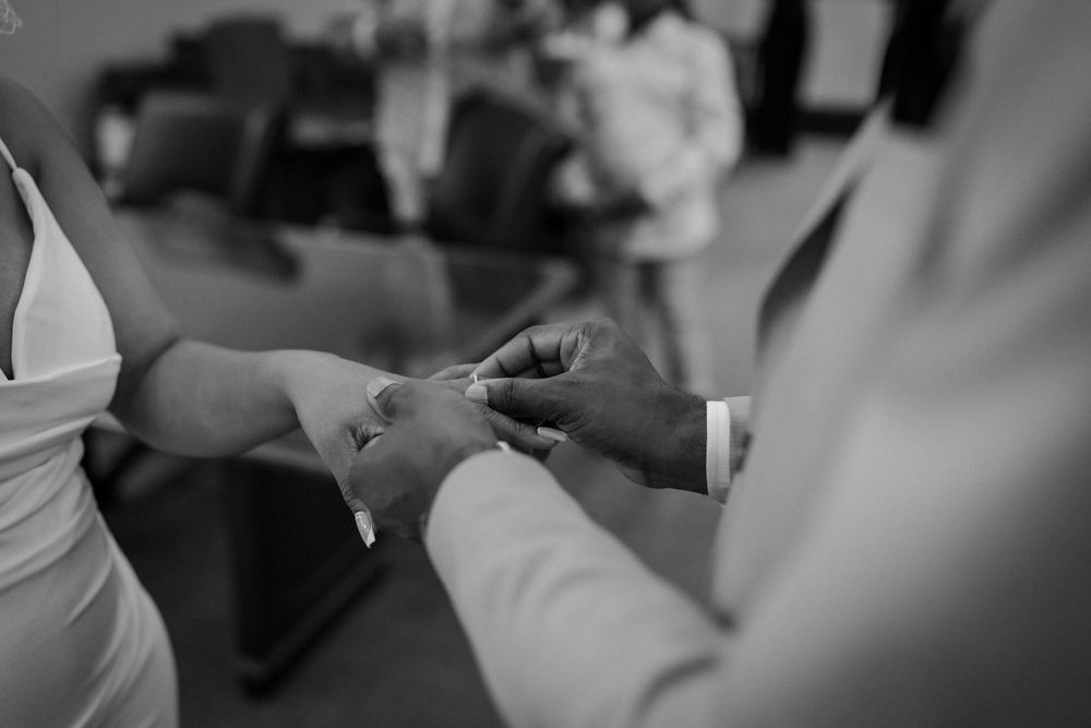 Black and white image capturing an emotional exchange of rings during a ceremony.