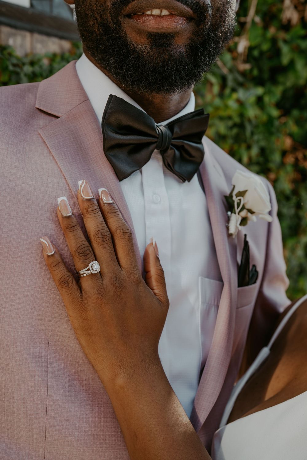 Close-up of wedding rings and formal attire details in pink and black.