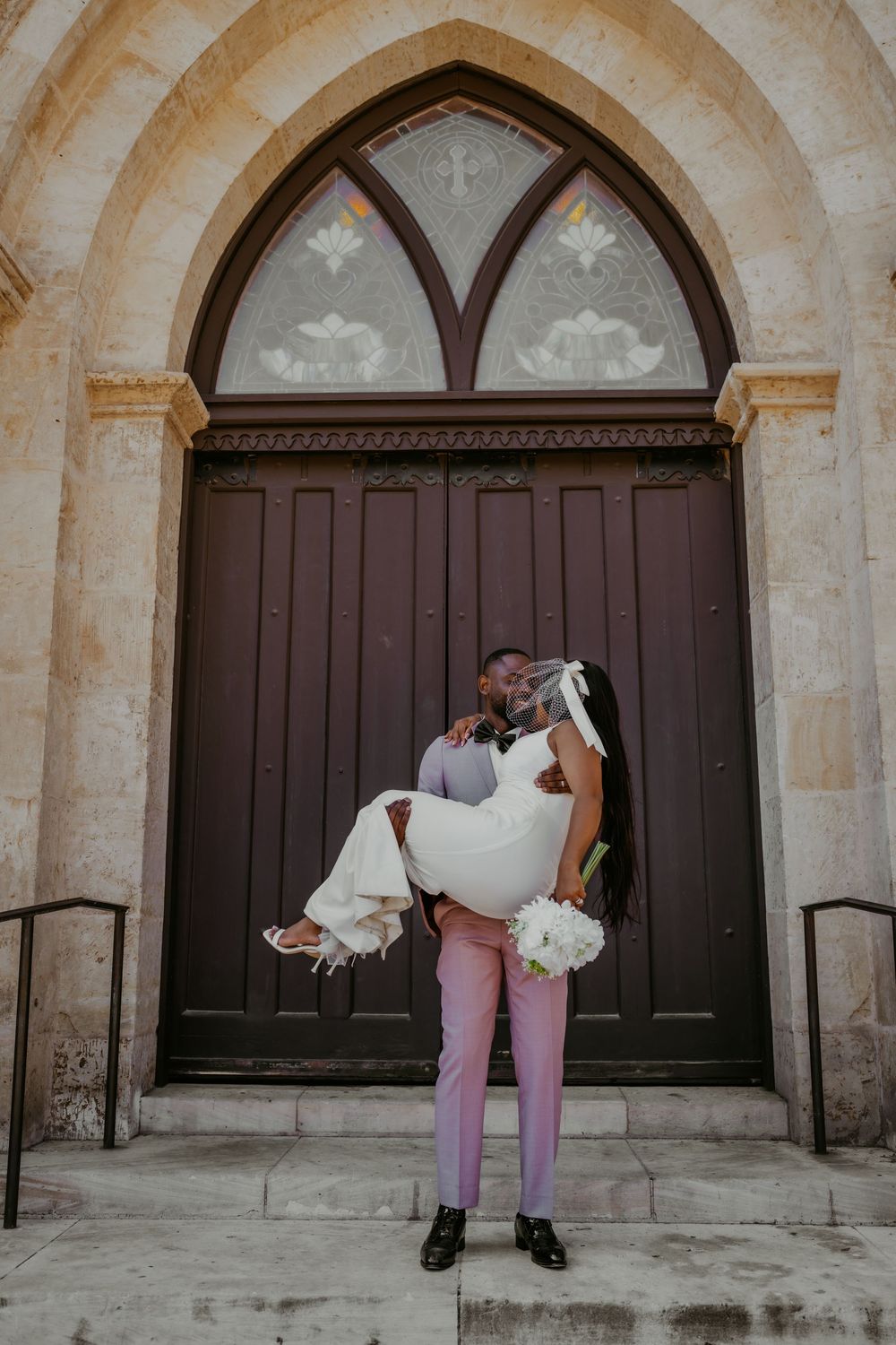 Romantic wedding portrait with couple embracing against ornate church architecture.