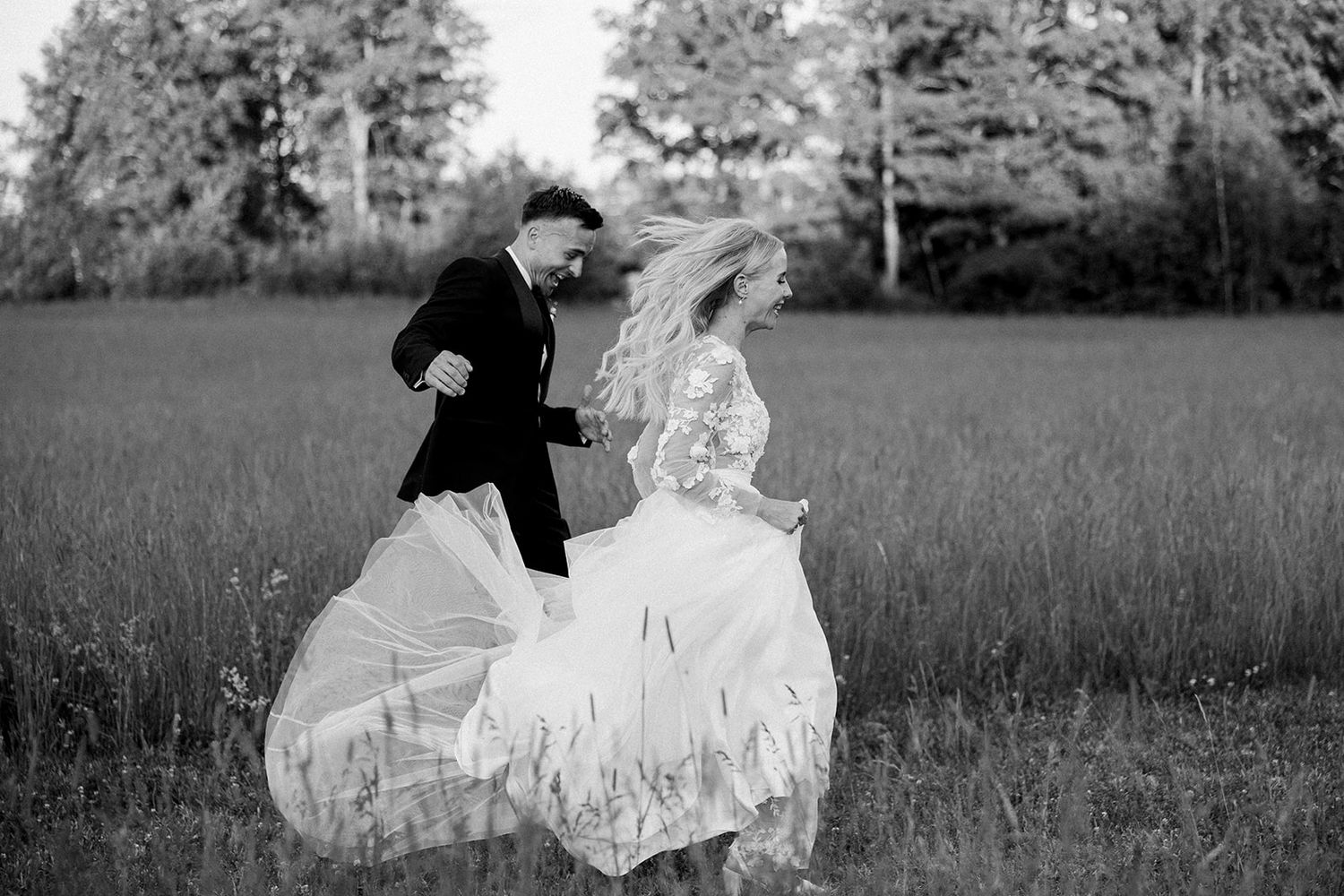 A couple in formal wedding attire poses together in a serene meadow during a black and white photo session.