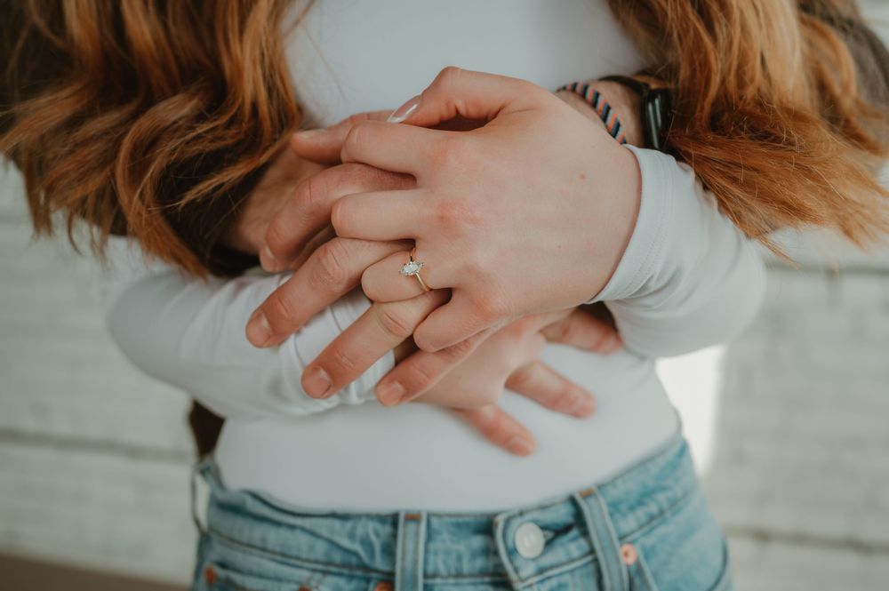 Close-up shot of hands with wedding rings against a rustic white brick wall background.