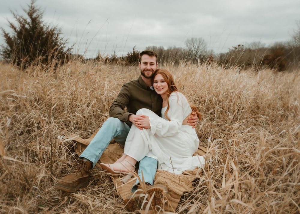 A couple sits together in a golden field of tall grass during sunset creating a romantic autumn scene.