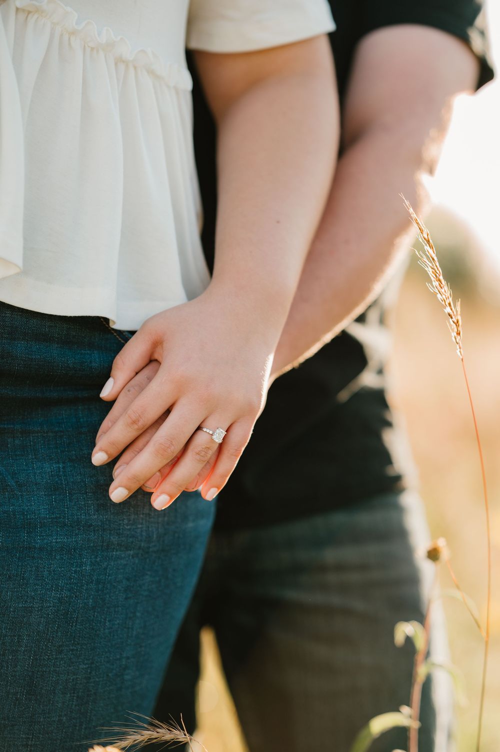 Close-up view of hands wearing a delicate gold ring against a soft backlit sunset background.