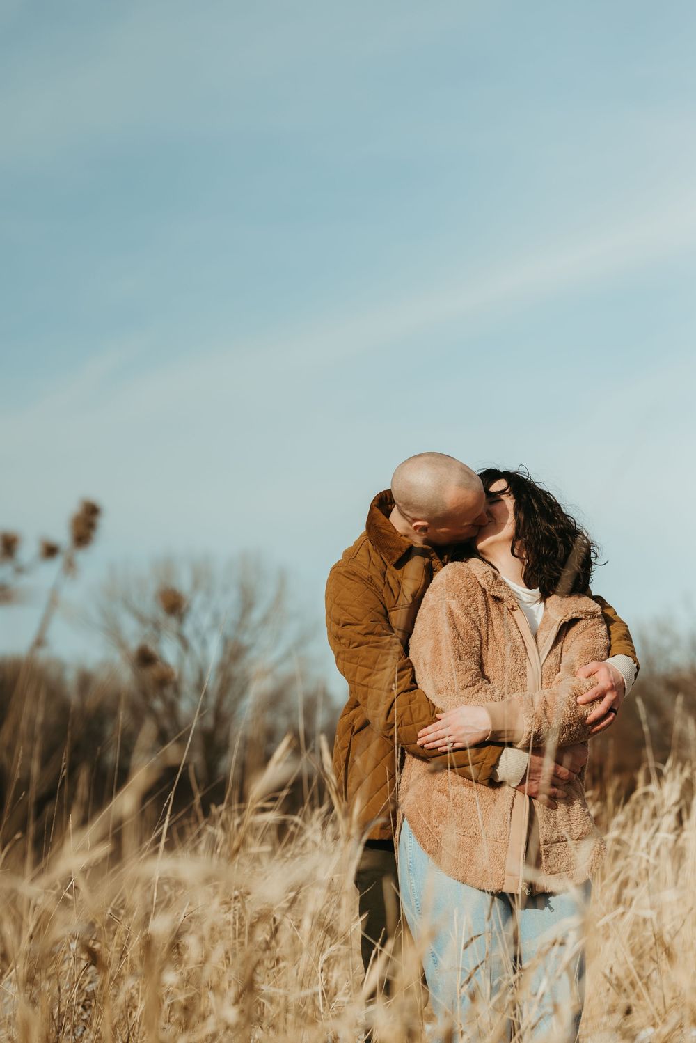 A couple embraces tenderly in a golden field of tall grass during sunset.