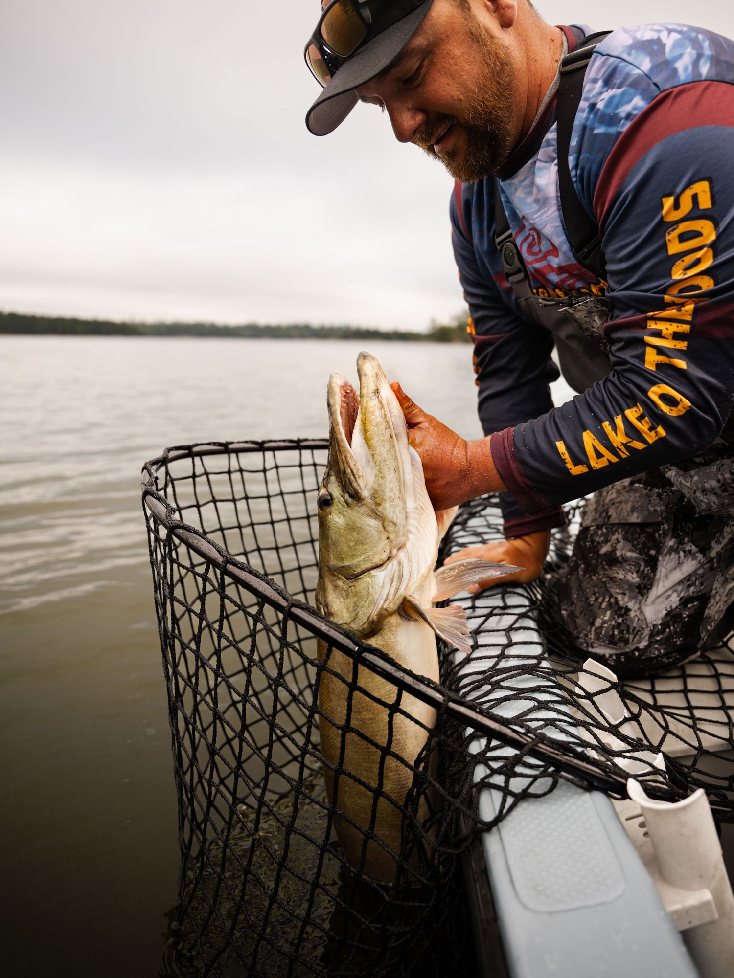 Fisherman holding freshly caught walleye in net over lake water.