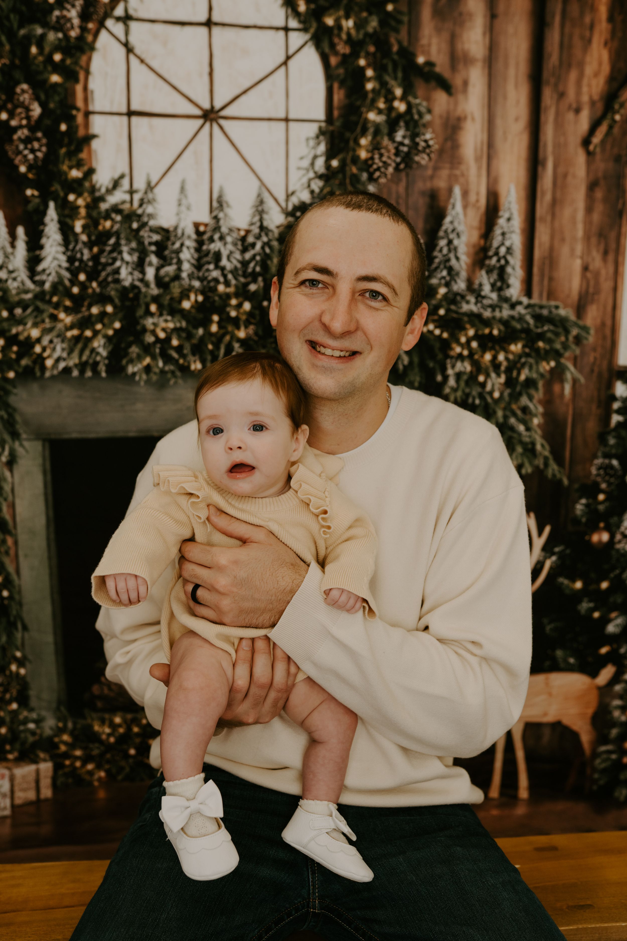 Indoor family portrait session with rustic wooden backdrop and greenery.