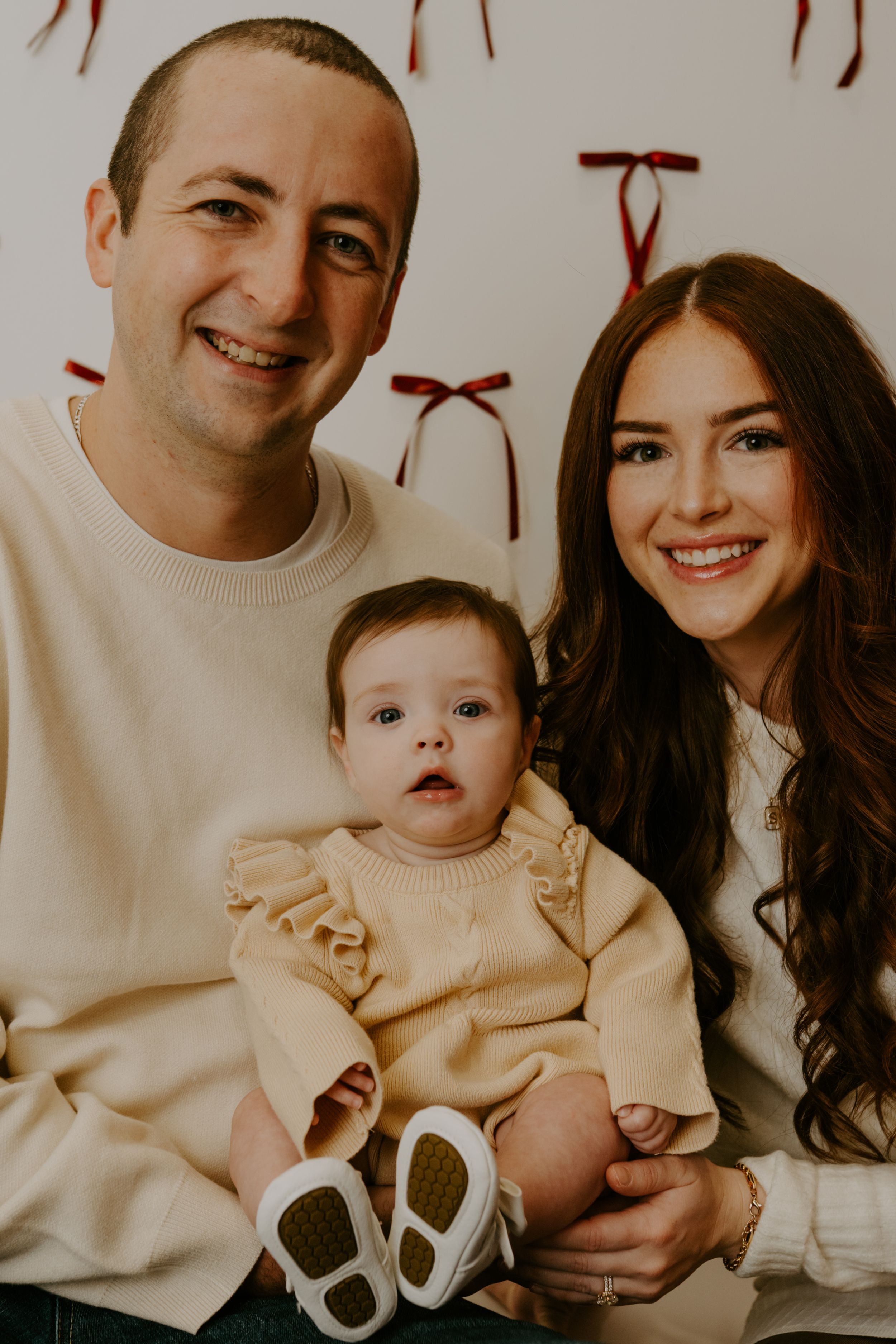 A family photo shoot featuring coordinated cream colored outfits against a light background.