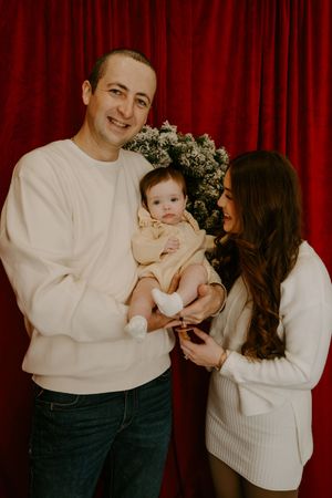 Family portrait session against a deep red curtain backdrop with white sweaters.