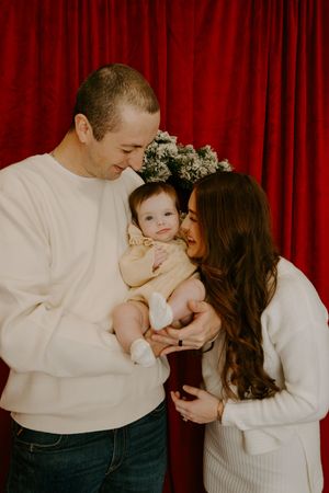 A loving family moment captured against a red curtain backdrop during a holiday photoshoot.