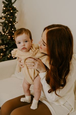 An intimate mother and baby portrait with a decorated Christmas tree in the background.