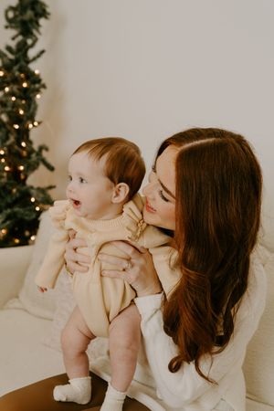 A joyful moment between parent and child beside a Christmas tree in a cozy living room setting.