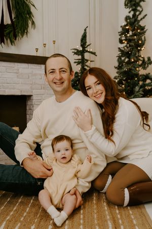 A family Christmas portrait by a white brick fireplace with festive decorations.