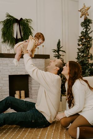 A playful family moment on the floor by a decorated fireplace during holiday season.