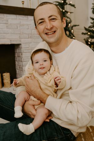 A cheerful holiday portrait by a decorated fireplace with warm lighting.
