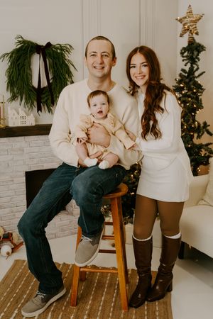A stylish family Christmas portrait featuring coordinated white outfits and holiday decor.