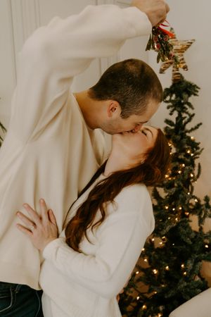 A romantic holiday moment under mistletoe with a Christmas tree in the background.