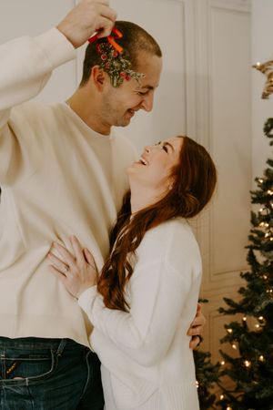 A playful couple laughs together near a decorated Christmas tree with mistletoe.