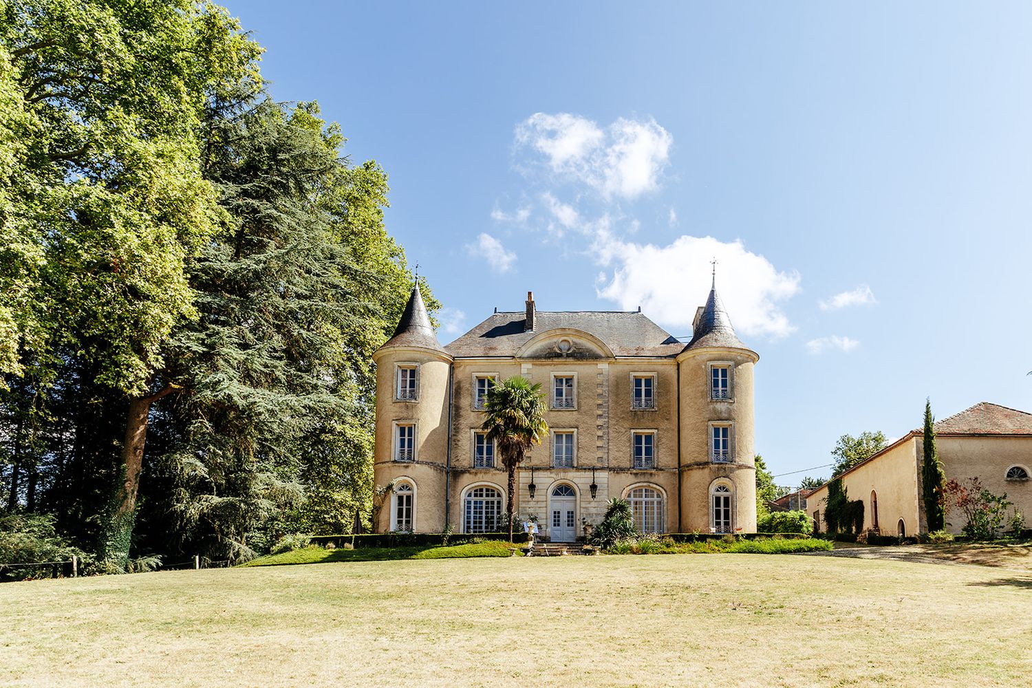 Panoramic view of a grand French chateau with classic architecture and symmetrical design set against a blue sky.