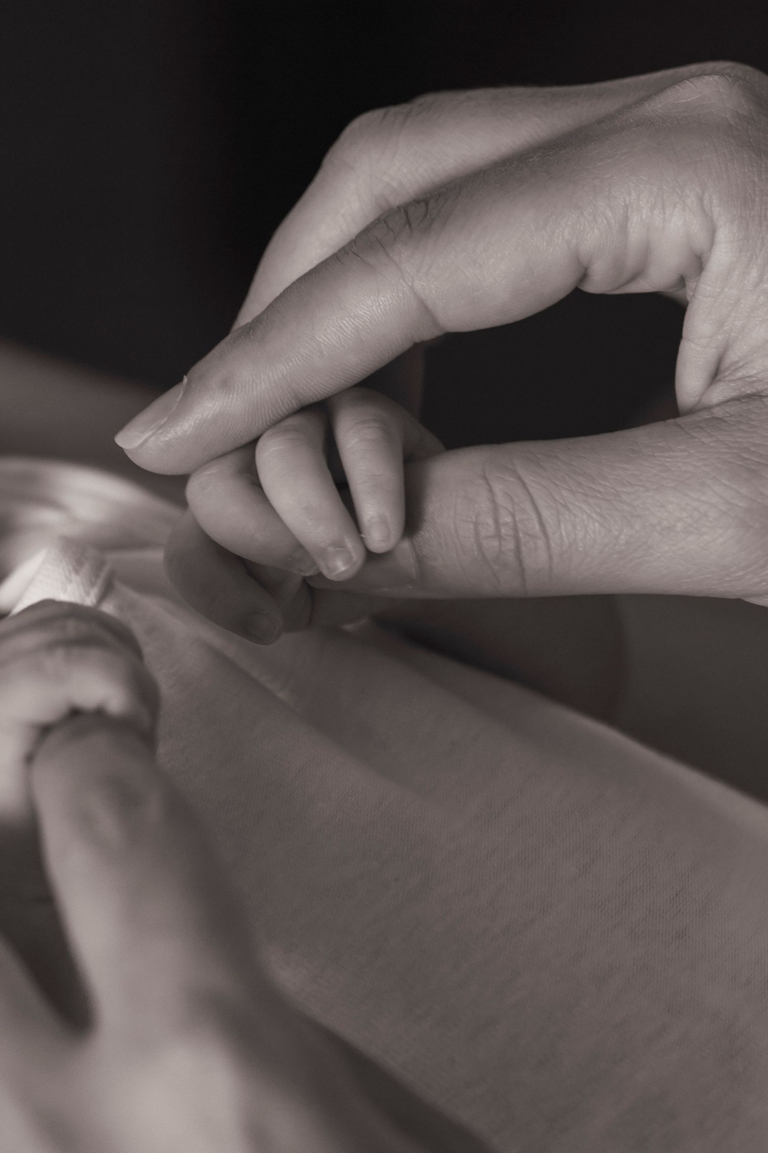 Newborn photography session. Close-up black and white image of gentle hands providing therapeutic touch.