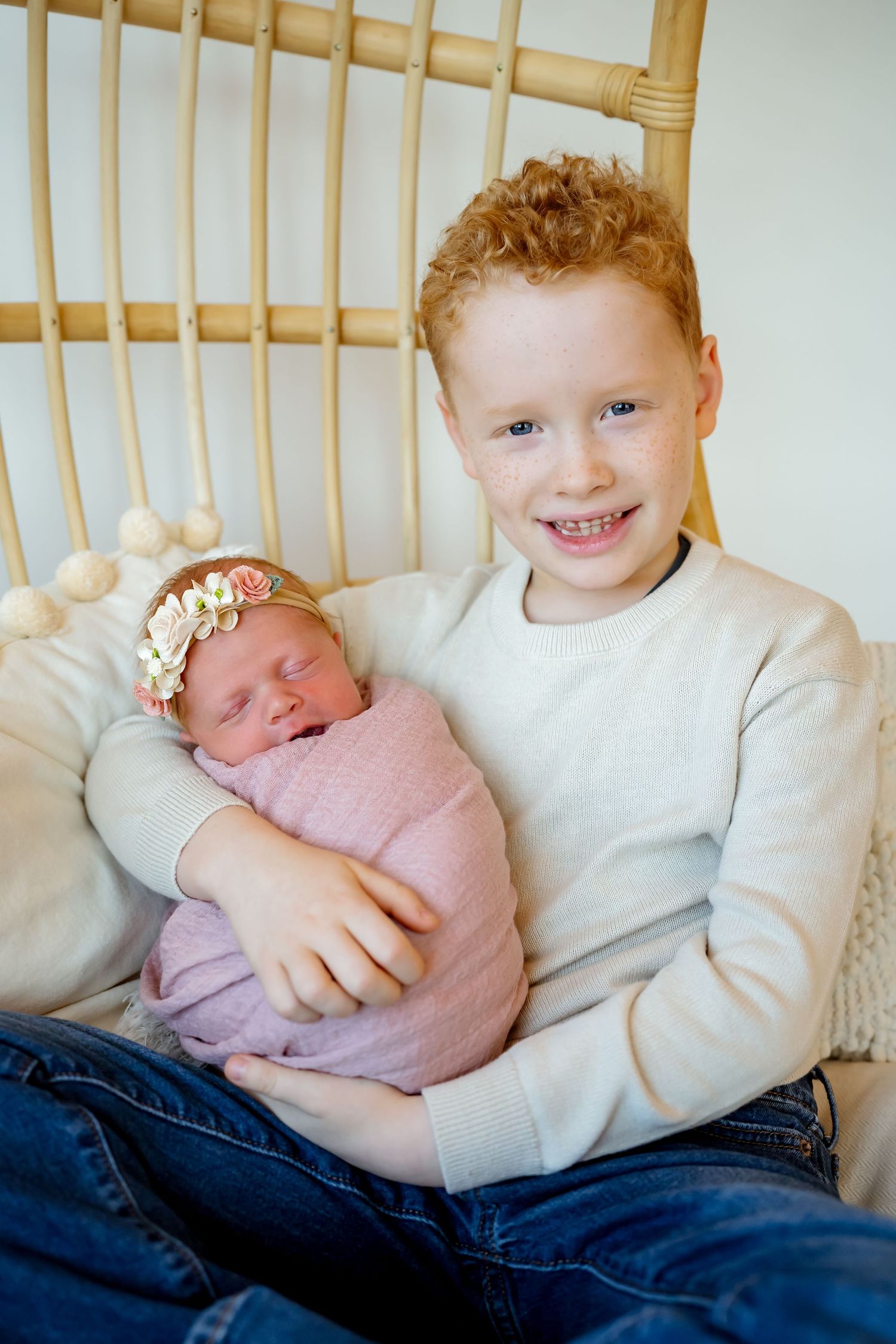 A series of sweet moments showing a child in a white sweater holding and cuddling with a newborn baby in pink.