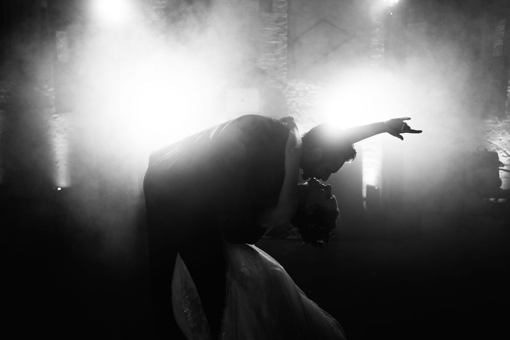 Silhouetted figures perform on a misty concert stage with dramatic backlighting creating an atmospheric effect.