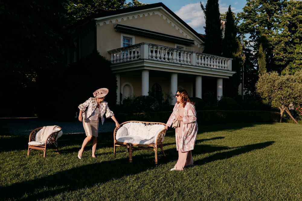 Two people enjoy a playful moment with a white blanket on a sunny grassy lawn near a house.