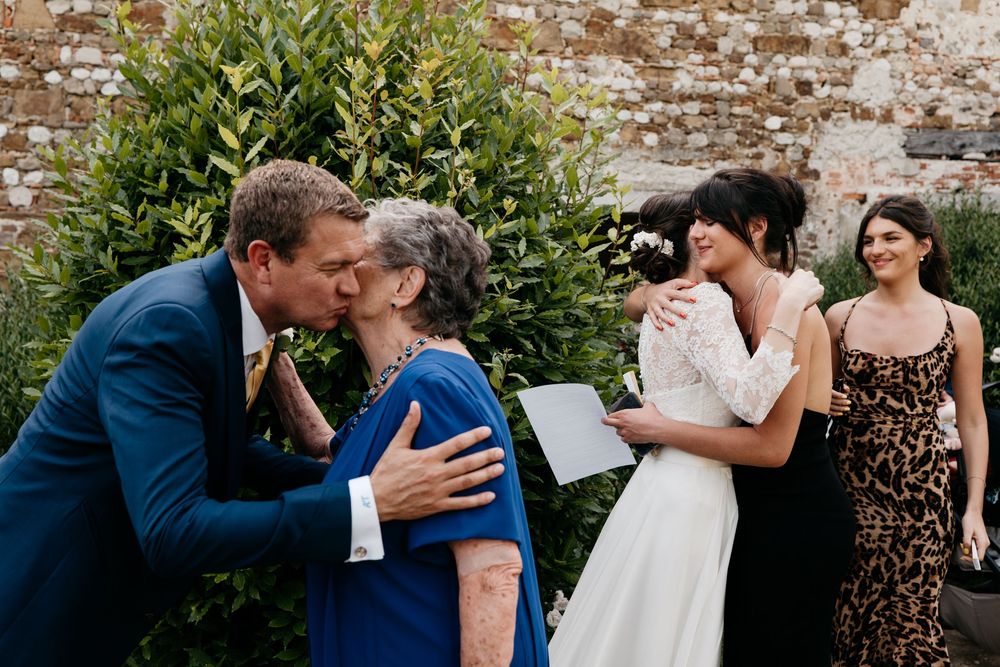 A joyful wedding celebration moment outdoors against a rustic brick wall with greenery.