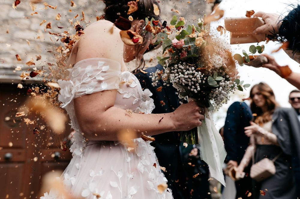 Wedding guests shower newlyweds with confetti and rose petals during outdoor celebration.