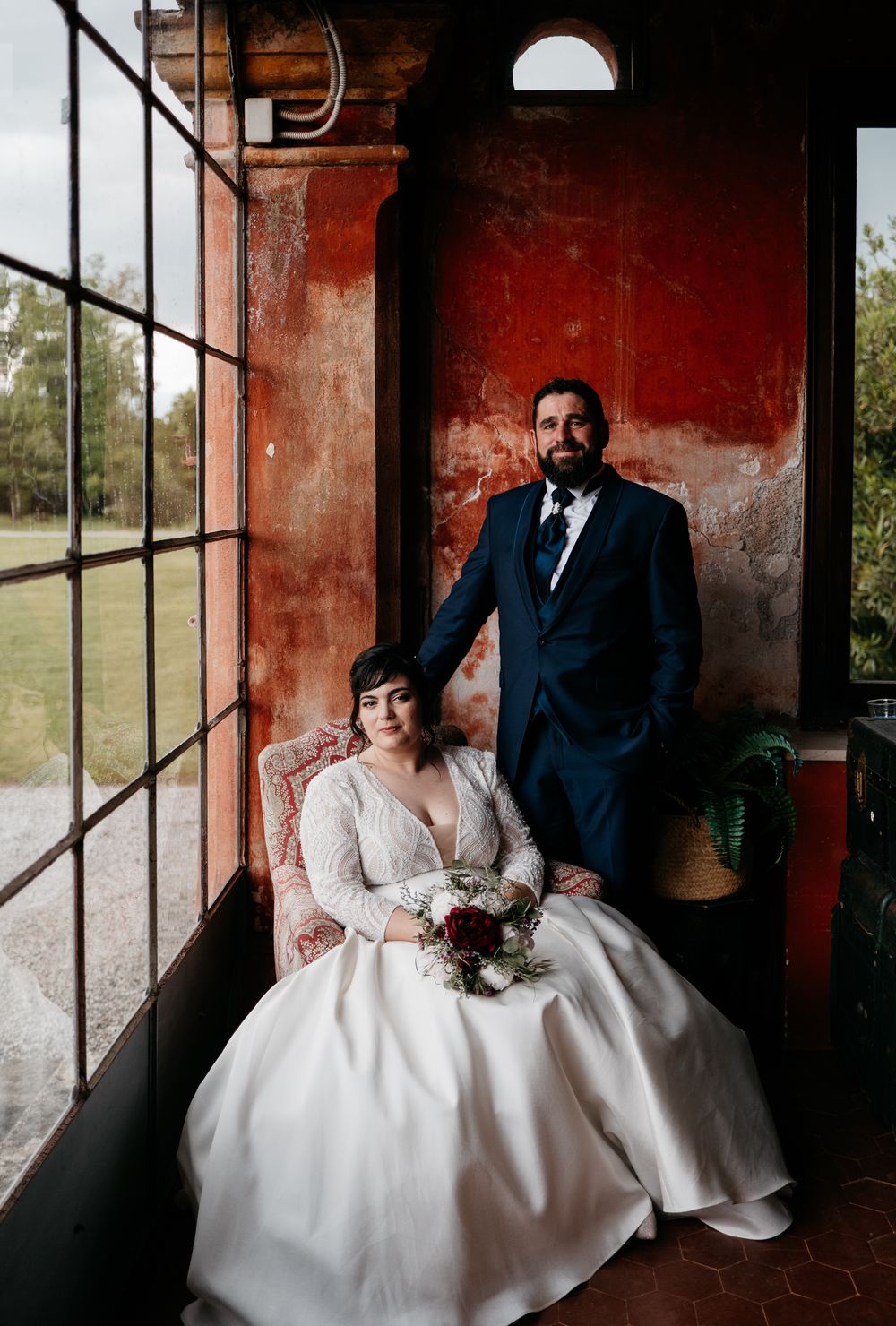 A romantic wedding photoshoot in a rustic red-walled room with large windows.