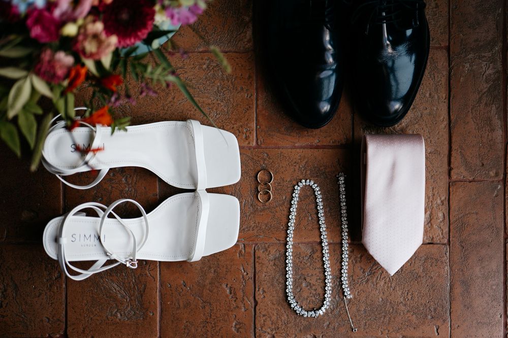 A collection of wedding accessories including shoes, ties, and jewelry arranged on a rustic wooden surface.