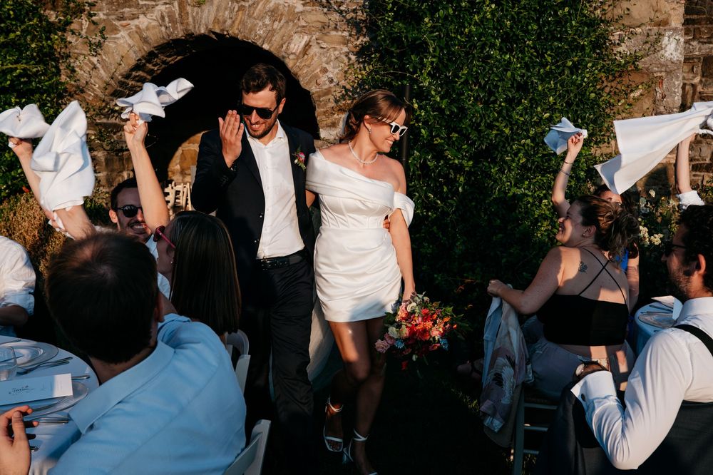Guests dancing and celebrating at an outdoor wedding reception under stone archways.