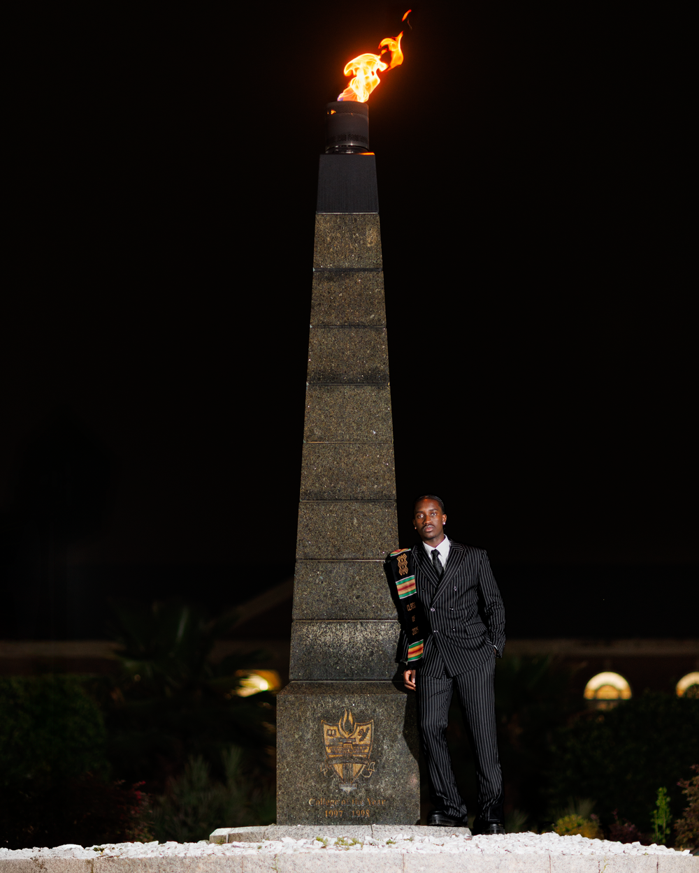 A sequence of photos shows a figure in a suit next to a stone obelisk monument with a flame burning at night.