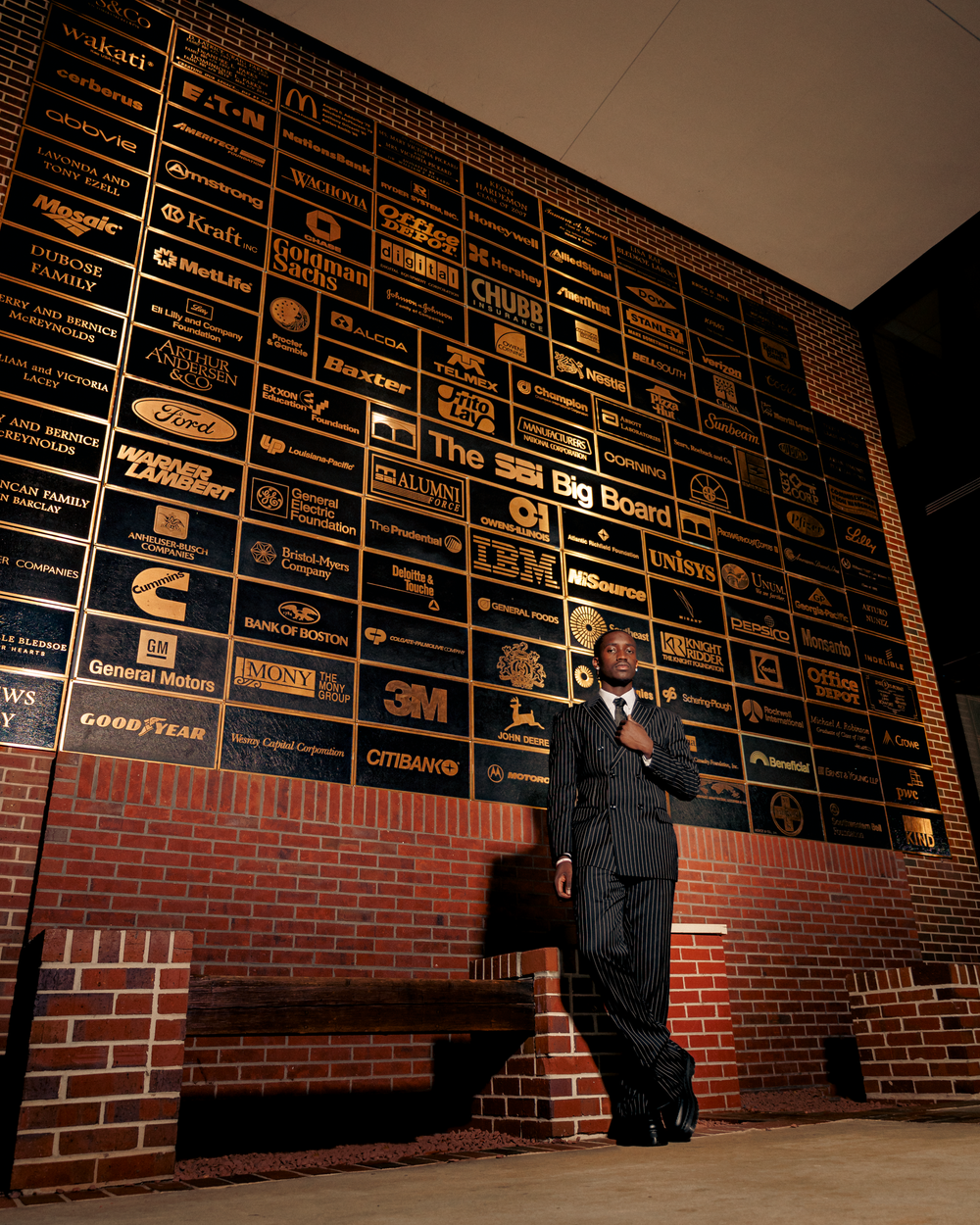 A dark corporate lobby wall featuring numerous illuminated company logos and brand names mounted on brick and black panels.