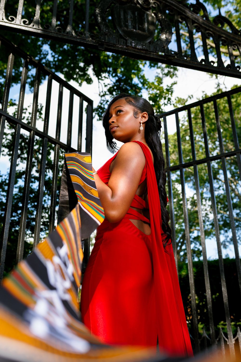 Person in a bright red dress stands against black metal railings while looking upward on a sunny day.