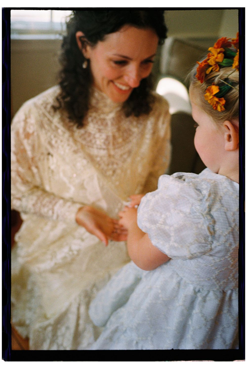 The bride and her flower girl getting dressed together in the afternoon sun before her wedding ceremony in a late summer meadow in Maine.