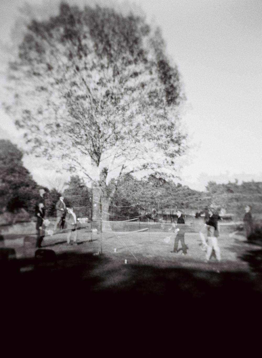 120mm double exposure black and white photograph of people playing badminton under a big tree after a wedding ceremony in southern Maine.