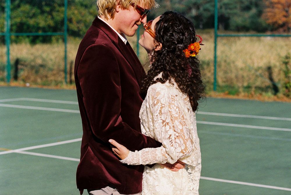 Landscape on 35mm color film of couple smiling each other right before a kiss. They are standing on an empty tennis court after marrying.