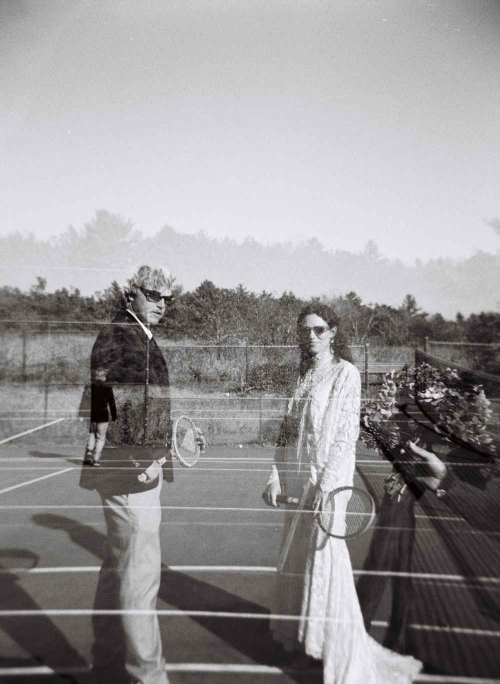 Black and white 120mm double exposure of the wedding couple on a tennis court with someone holding out the bouquet in Kennebunk, Maine.