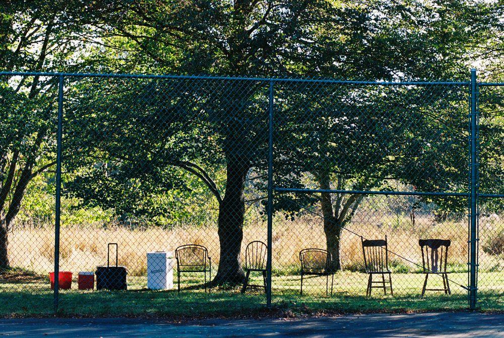 35mm color photograph of various chairs set up outside of the tennis court under a tree for guests during a wedding reception in Maine.