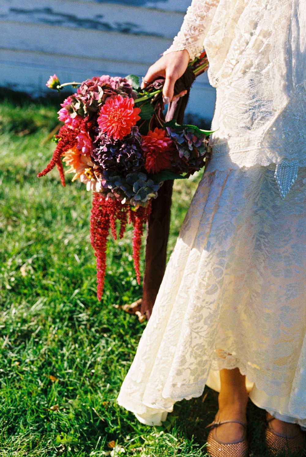 Detail of the bride holding her floral bouquet down by her side in front of the green grass after her wedding ceremony in southern Maine.
