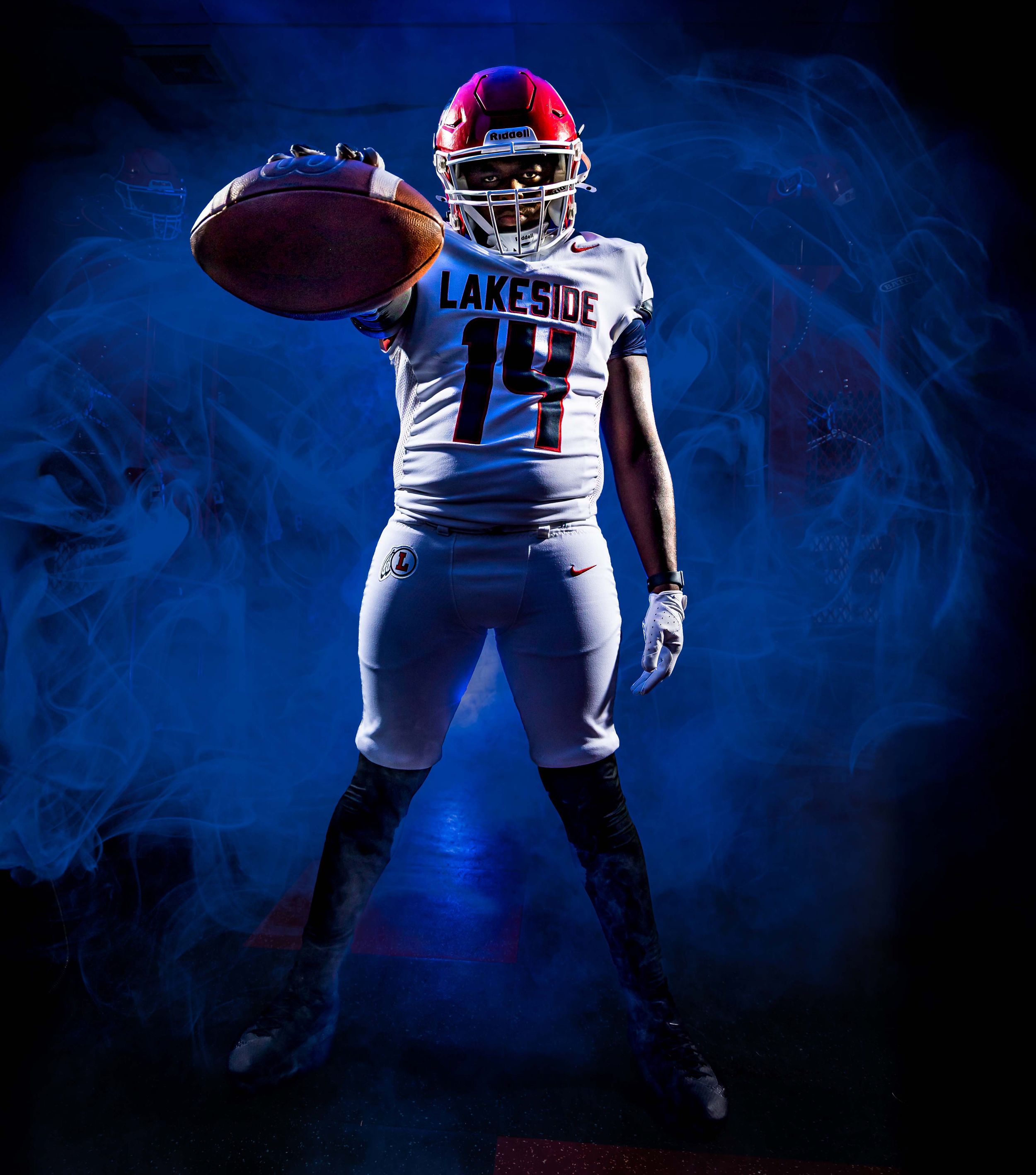 Football player in blue and red uniform making a dramatic catch against dark background with moody lighting.