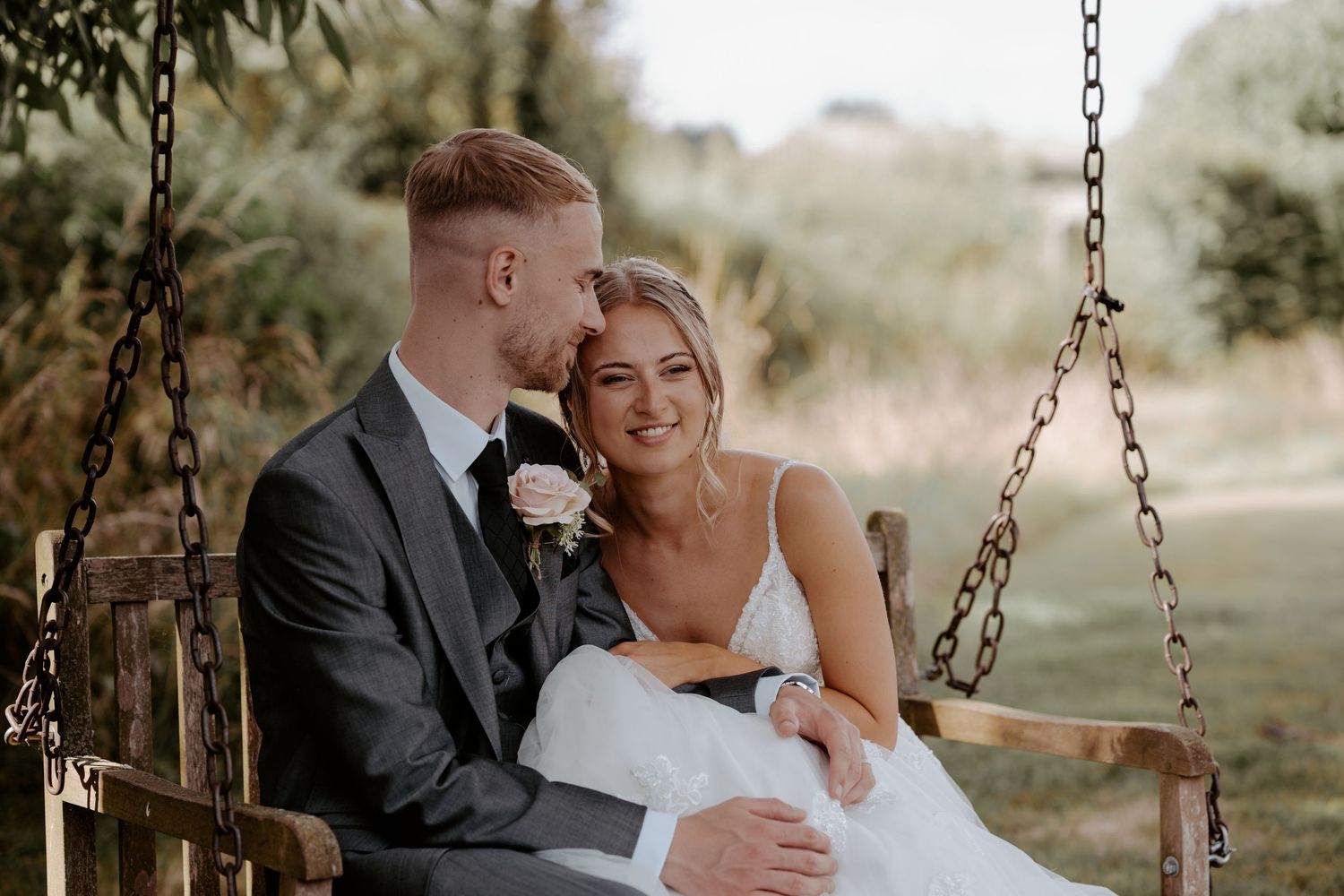 A couple stands in an arched brick doorway with rustic wooden doors opened wide on their wedding day.