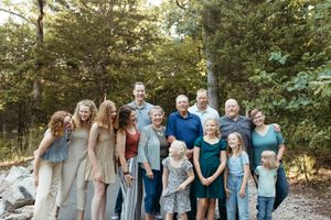 A large group of people wearing coordinated blue and gray outfits pose together outdoors in a wooded setting.