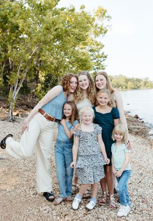 A group poses together on a rocky beach near trees during a casual outdoor photo session.