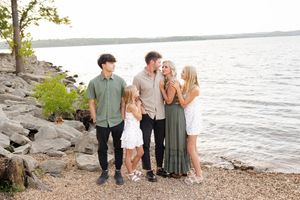 A family in coordinating outfits walks along a rocky beach shoreline at sunset.
