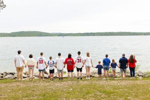 Group of people sitting in chairs on a beach overlooking a calm lake with distant shoreline visible.