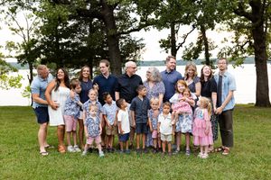 Large extended family group gathered outdoors for a casual summer photo session in a grassy park setting.
