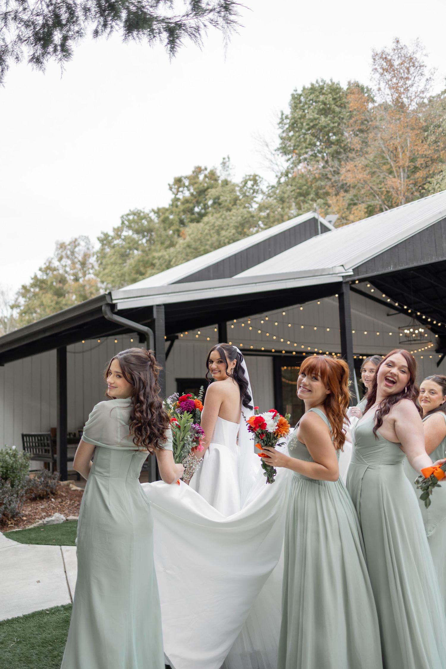 Bridesmaids in sage green dresses help adjust a wedding dress train in at FIREFLY LANE nashville tennessee photographer firefly lane barn