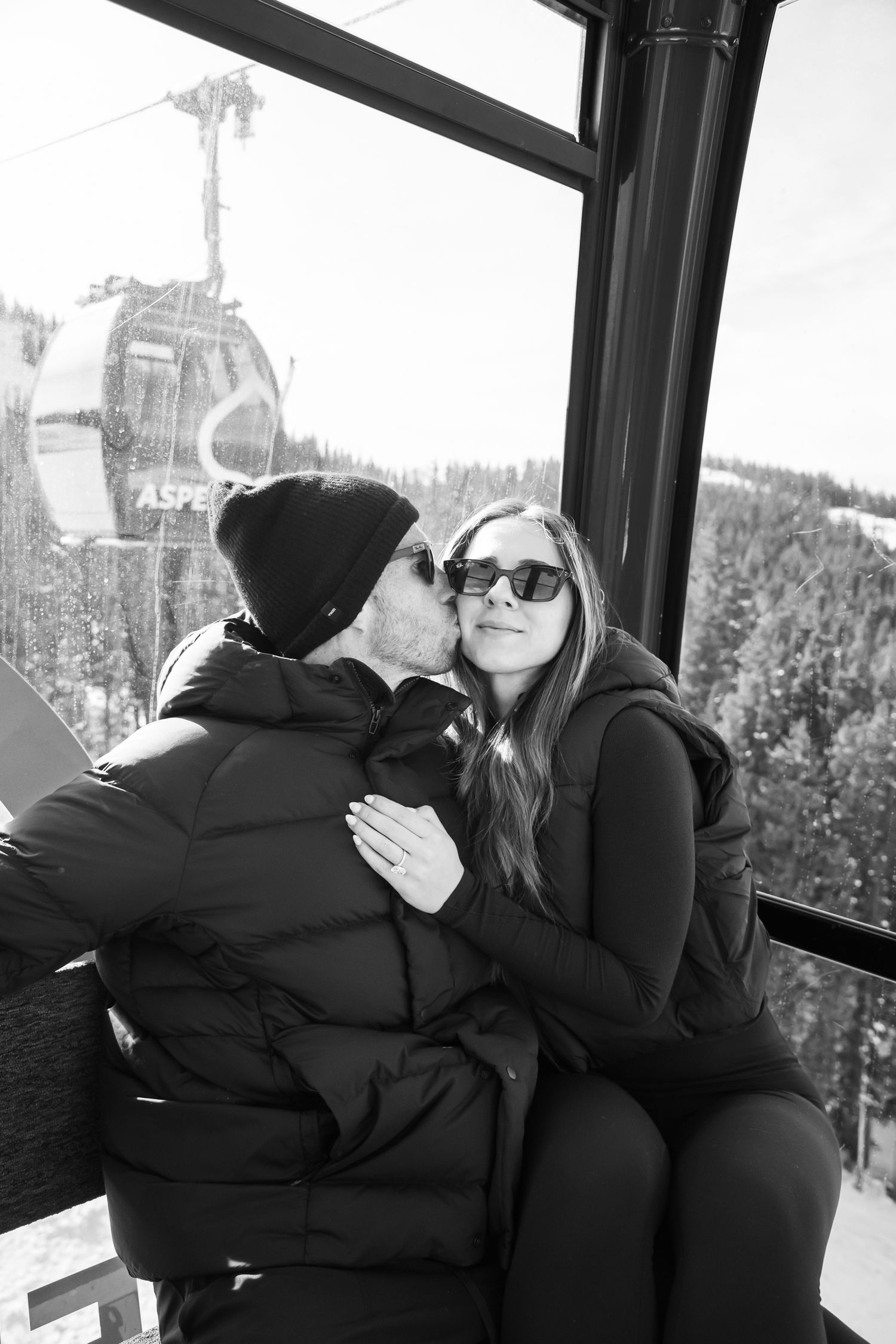 Stylish young couple cuddles as they ride the gondola down in Aspen after a mountain top proposal