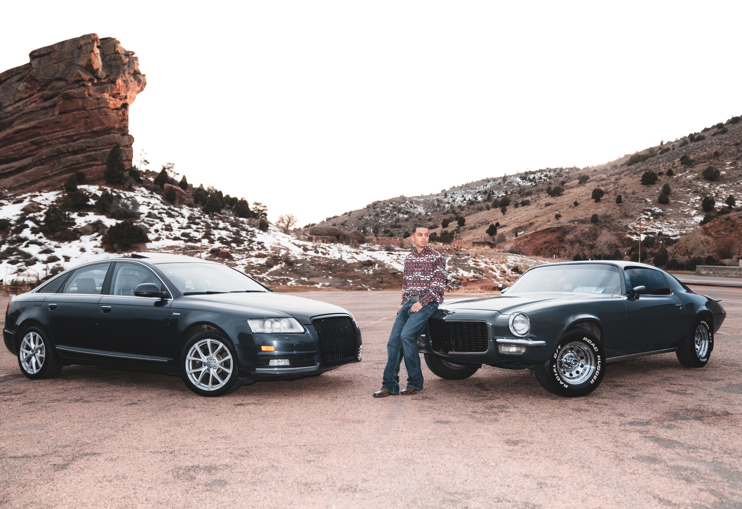 Two Audi sedans parked in front of a rocky mountain landscape with patches of snow visible in the background.